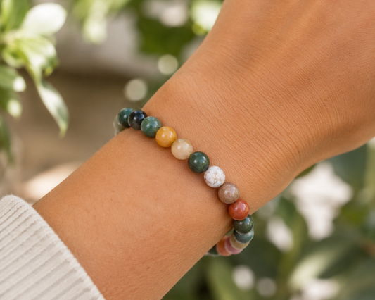 Bracelet en Agate Indienne porté au poignet, avec perles multicolores en pierre naturelle devant un décor végétal doux.