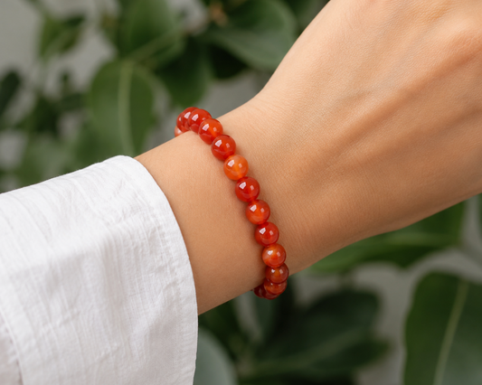 Bracelet en Agate rubanée traitée rouge porté au poignet, avec perles rouges et orangées dans un décor végétal.