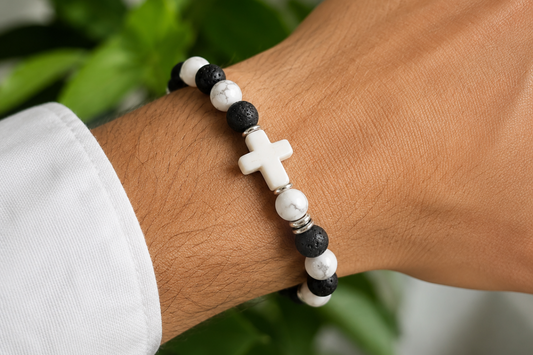Bracelet Howlite et Pierre de Lave avec croix blanche porté au poignet, avec perles blanches veinées, perles noires texturées et détails métal.