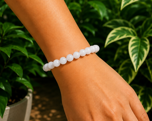 Bracelet en Jade Blanc naturel porté au poignet, avec perles blanches lumineuses devant un décor végétal.
