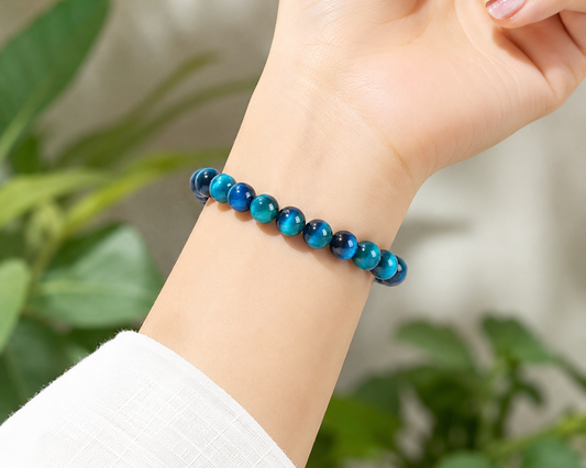 Bracelet en Œil de Faucon porté au poignet, avec perles bleues aux reflets chatoyants devant un décor végétal.