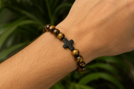 Bracelet en Œil de Tigre avec croix noire porté au poignet, avec perles brunes et dorées aux reflets chatoyants.