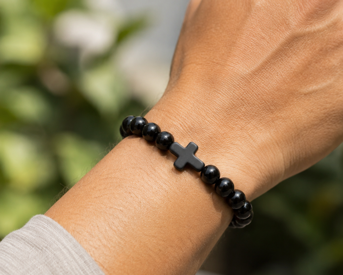 Bracelet en Onyx Noir avec croix noire porté au poignet, perles brillantes en pierre naturelle dans un style sobre et élégant.