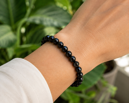 Bracelet en Agate naturelle traitée noire porté au poignet, avec perles noires brillantes dans un décor végétal.