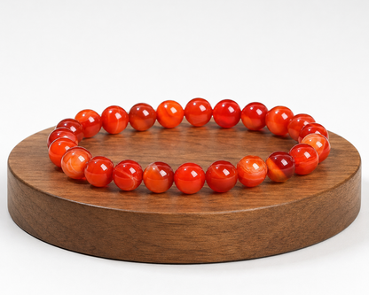 Bracelet en Agate rubanée traitée rouge présenté sur un socle en bois, avec perles rouges et orangées sur fond blanc.