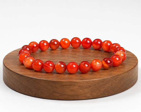 Bracelet en Agate rubanée traitée rouge présenté sur un socle en bois, avec perles rouges et orangées sur fond blanc.