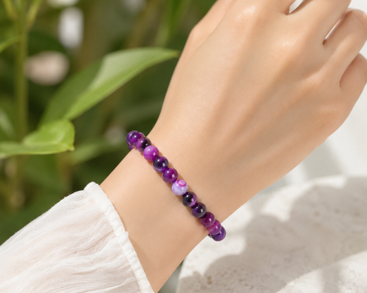 Bracelet en Agate rubanée traitée violette porté au poignet, avec perles brillantes dans un décor végétal.