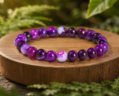 Bracelet en Agate rubanée traitée violette sur un socle en bois, avec perles marbrées dans un décor végétal.