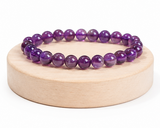 Bracelet en Améthyste présenté sur un socle en bois fond blanc, avec perles violettes en pierre naturelle aux reflets brillants.