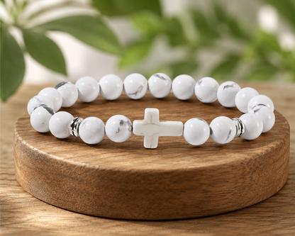 Bracelet en Howlite blanche avec croix blanche présenté sur un socle en bois, avec perles blanches veinées dans un décor végétal.