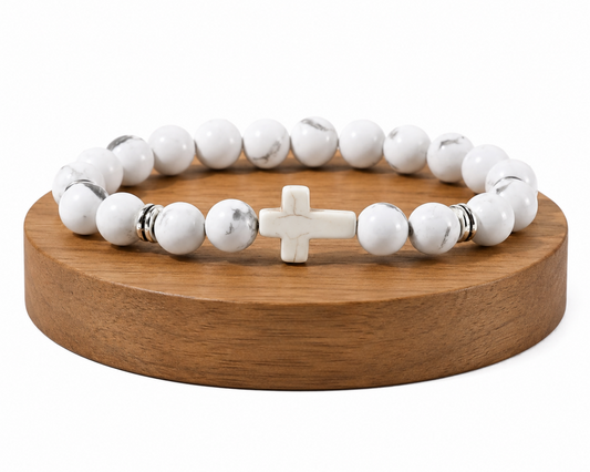 Bracelet en Howlite blanche avec croix blanche présenté sur un socle en bois fond blanc, avec perles blanches veinées et détails métal.