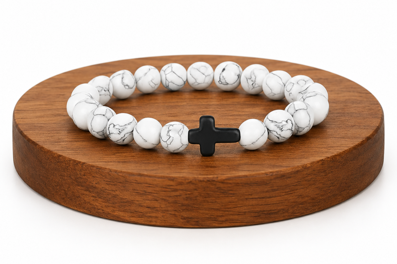 Bracelet en Howlite blanche avec croix noire présenté sur un socle en bois fond blanc, avec perles blanches veinées.