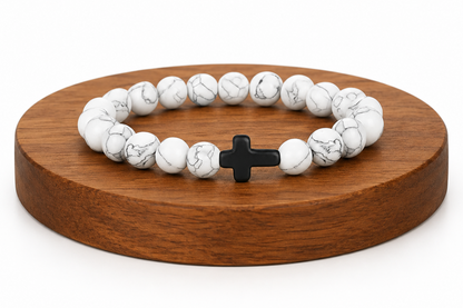 Bracelet en Howlite blanche avec croix noire présenté sur un socle en bois fond blanc, avec perles blanches veinées.