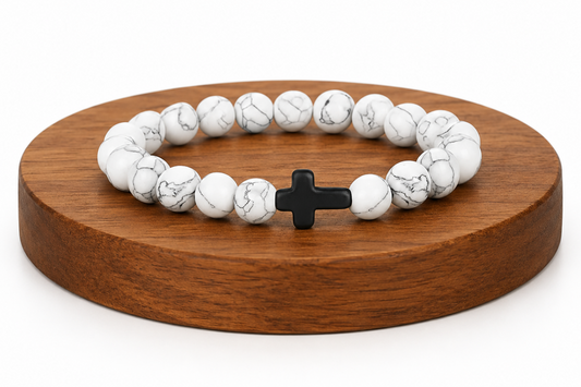 Bracelet en Howlite blanche avec croix noire présenté sur un socle en bois fond blanc, avec perles blanches veinées.