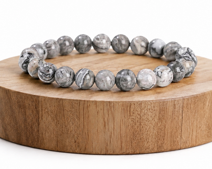 Bracelet en Jaspe Picasso présenté sur un socle en bois fond blanc, avec perles grises en pierre naturelle aux motifs marbrés.