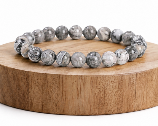 Bracelet en Jaspe Picasso présenté sur un socle en bois fond blanc, avec perles grises en pierre naturelle aux motifs marbrés.