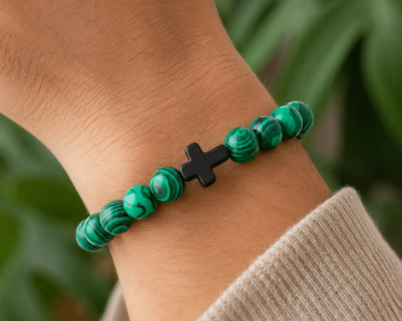 Bracelet en Malachite avec croix noire porté au poignet, perles vertes en pierre naturelle aux veines marbrées.