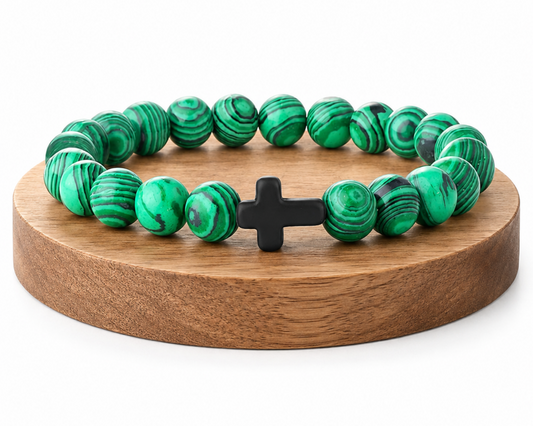 Bracelet en Malachite avec croix noire, perles vertes en pierre naturelle aux veines marbrées, présenté sur un socle en bois fond blanc.