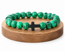 Bracelet en Malachite avec croix noire, perles vertes en pierre naturelle aux veines marbrées, présenté sur un socle en bois fond blanc.