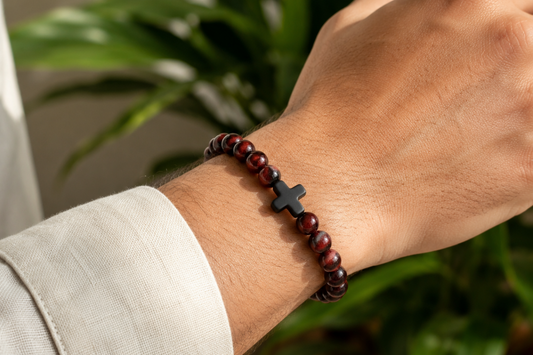 Bracelet en Œil de Taureau avec croix noire porté au poignet, avec perles brunes et rouges aux reflets chatoyants.