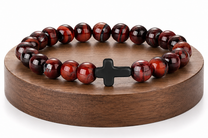 Bracelet en Œil de Taureau avec croix noire présenté sur un socle en bois fond blanc, avec perles brunes et rouges aux reflets brillants.