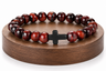 Bracelet en Œil de Taureau avec croix noire présenté sur un socle en bois fond blanc, avec perles brunes et rouges aux reflets brillants.