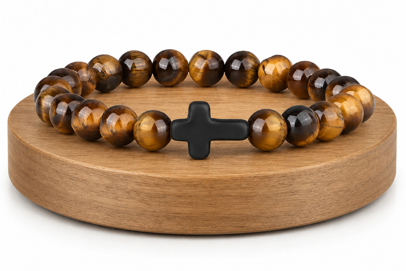 Bracelet en Œil de Tigre avec croix noire présenté sur un socle en bois fond blanc, avec perles brunes et dorées aux reflets chatoyants.