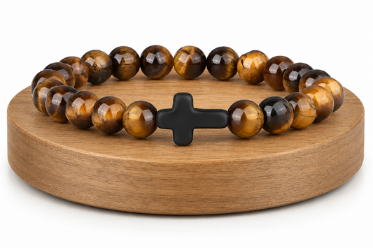 Bracelet en Œil de Tigre avec croix noire présenté sur un socle en bois fond blanc, avec perles brunes et dorées aux reflets chatoyants.