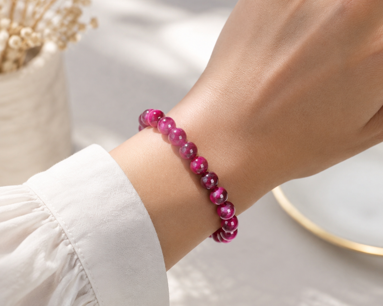 Bracelet en Œil de Tigre traité fuchsia porté au poignet, avec perles roses aux reflets chatoyants.