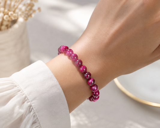 Bracelet en Œil de Tigre traité fuchsia porté au poignet, avec perles roses aux reflets chatoyants.