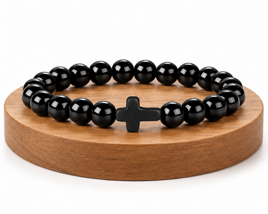 Bracelet en Onyx Noir avec croix noire, perles brillantes en pierre naturelle, présenté sur un socle en bois fond blanc.