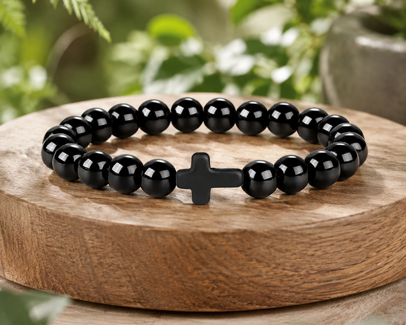 Bracelet en Onyx Noir avec croix noire, perles brillantes en pierre naturelle, présenté sur un socle en bois avec décor végétal.