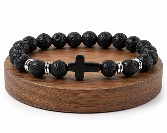 Bracelet en Pierre de Lave avec croix noire et perles métal, présenté sur un socle en bois fond blanc avec perles noires texturées.