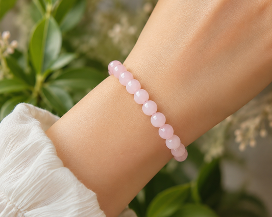 Bracelet en Quartz Rose porté au poignet, avec perles rose pâle en pierre naturelle devant un décor végétal doux.