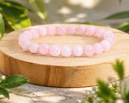 Bracelet en Quartz Rose présenté sur un socle en bois, avec perles rose pâle en pierre naturelle dans un décor végétal doux.