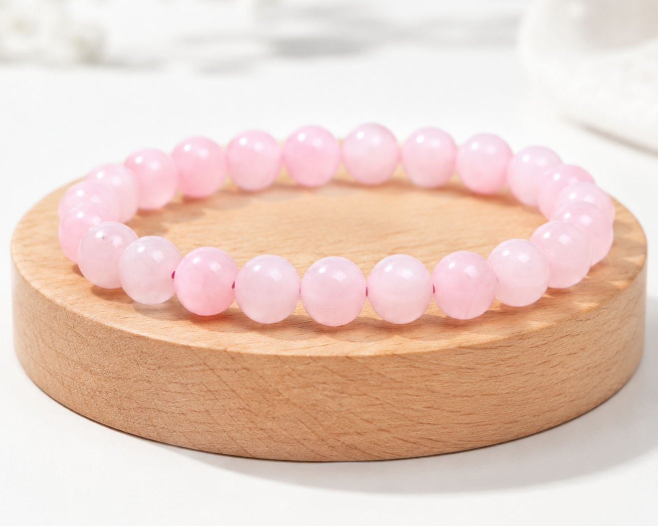 Bracelet en Quartz Rose présenté sur un socle en bois fond clair, avec perles rose pâle en pierre naturelle aux reflets doux.