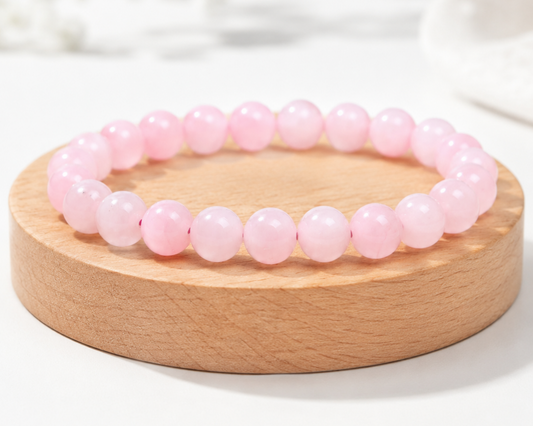 Bracelet en Quartz Rose présenté sur un socle en bois fond clair, avec perles rose pâle en pierre naturelle aux reflets doux.
