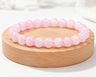 Bracelet en Quartz Rose présenté sur un socle en bois fond clair, avec perles rose pâle en pierre naturelle aux reflets doux.
