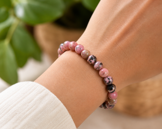 Bracelet en Rhodonite porté au poignet, avec perles roses et noires en pierre naturelle devant un décor végétal doux.
