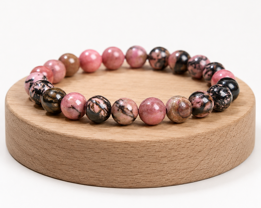 Bracelet en Rhodonite présenté sur un socle en bois fond blanc, avec perles roses et noires en pierre naturelle.