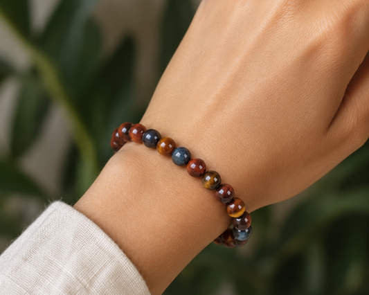 Bracelet triple protection porté au poignet, avec perles en Œil de Tigre, Œil de Taureau et Œil de Faucon devant un décor végétal.